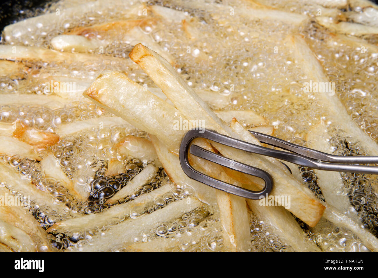 Moyennes pommes de terre Russet pelés, tranchés et la poêle dans l'huile chaude de la création home made French Fries, en remuant en cours de cuisson avec des pinces. Un peu coûteux Banque D'Images