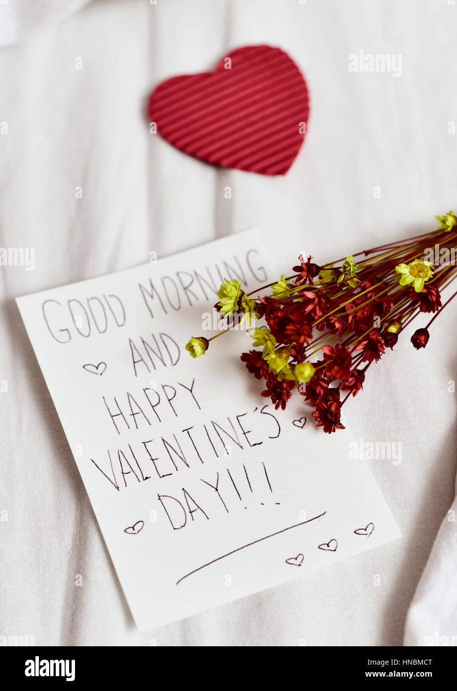 Libre d'un livre blanc remarque avec le texte Bonjour et happy valentines day écrit en C, un cœur rouge et un bouquet de fleurs séchées, sur la whit Banque D'Images