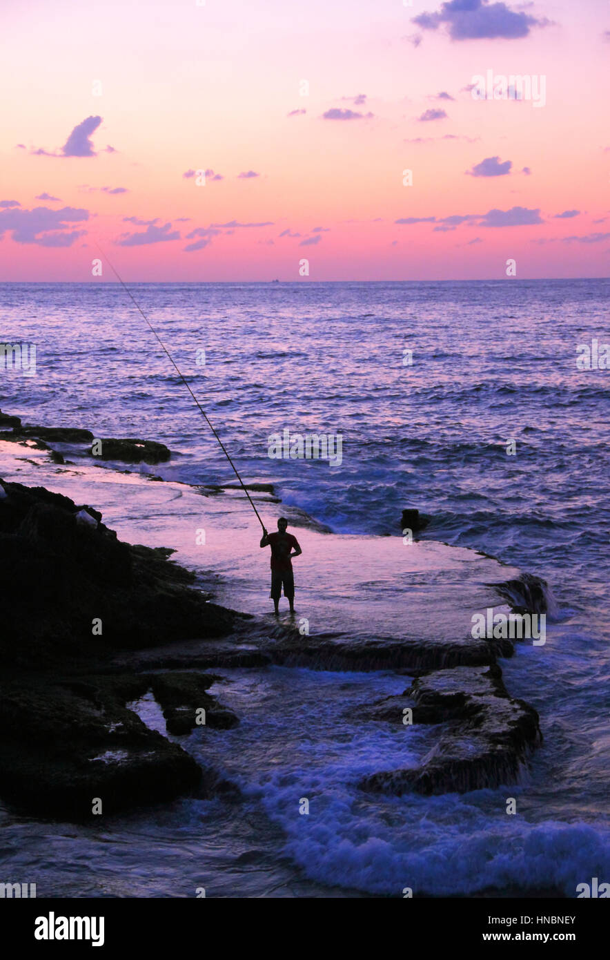 Un pêcheur solitaire jette sa canne le long du littoral méditerranéen Beyrouth rocheux au coucher du soleil, le Liban. Banque D'Images