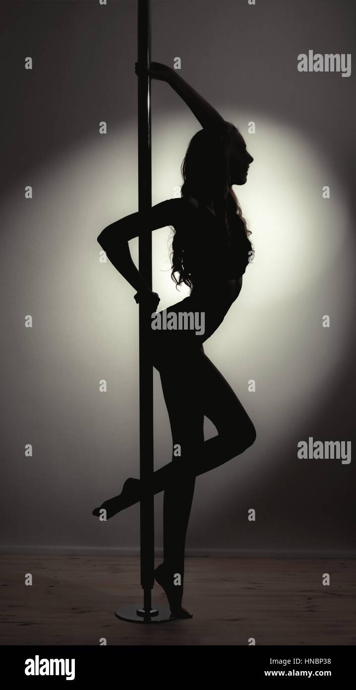 Silhouette de jeune femme slim fit pole dancer avec de très longs cheveux contre poteau avec Spotlight dans l'arrière-plan de la création d'une forme dramatique et pose Banque D'Images