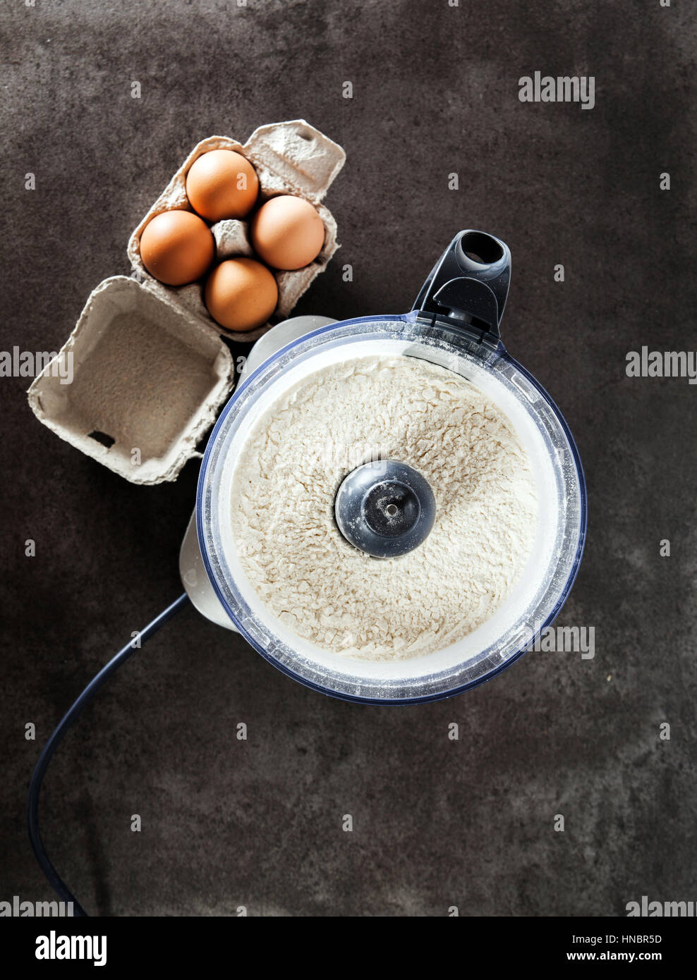 Préparer la pâte à partir de l'oeufs dans le processeur de nourriture sur la table en pierre grise Banque D'Images