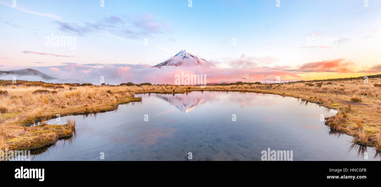 Reflet dans le lac rose Pouakai Tarn, nuages autour du Mont Taranaki ou Mont stratovolcan Egmont au coucher du soleil, Parc National d'Egmont Banque D'Images