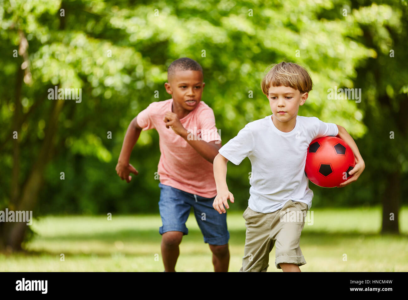 Deux courses de garçon dans le parc de ballon de soccer en été Banque D'Images