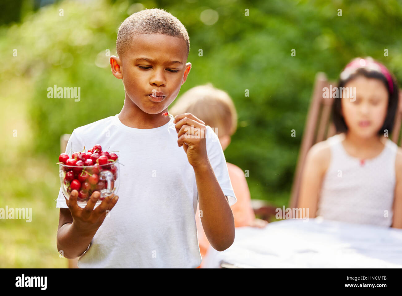 Enfant Africain grignoter sain et délicieux les cerises au jardin Banque D'Images