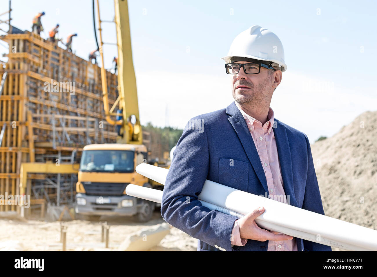 Confiant architect holding rolled up blueprints at construction site Banque D'Images