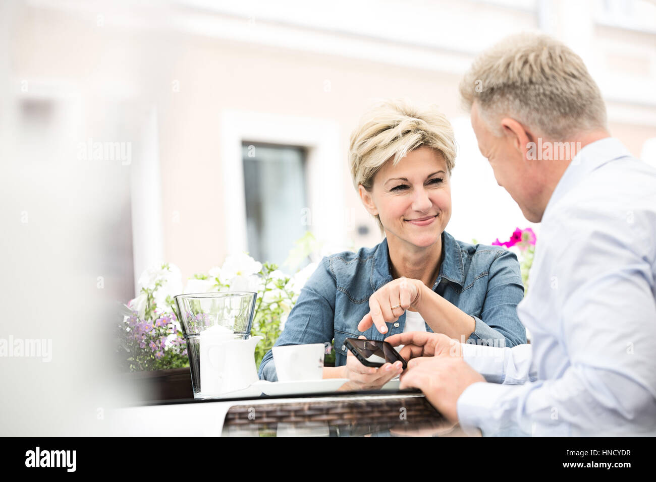 Happy middle-aged woman using cell phone at sidewalk cafe Banque D'Images