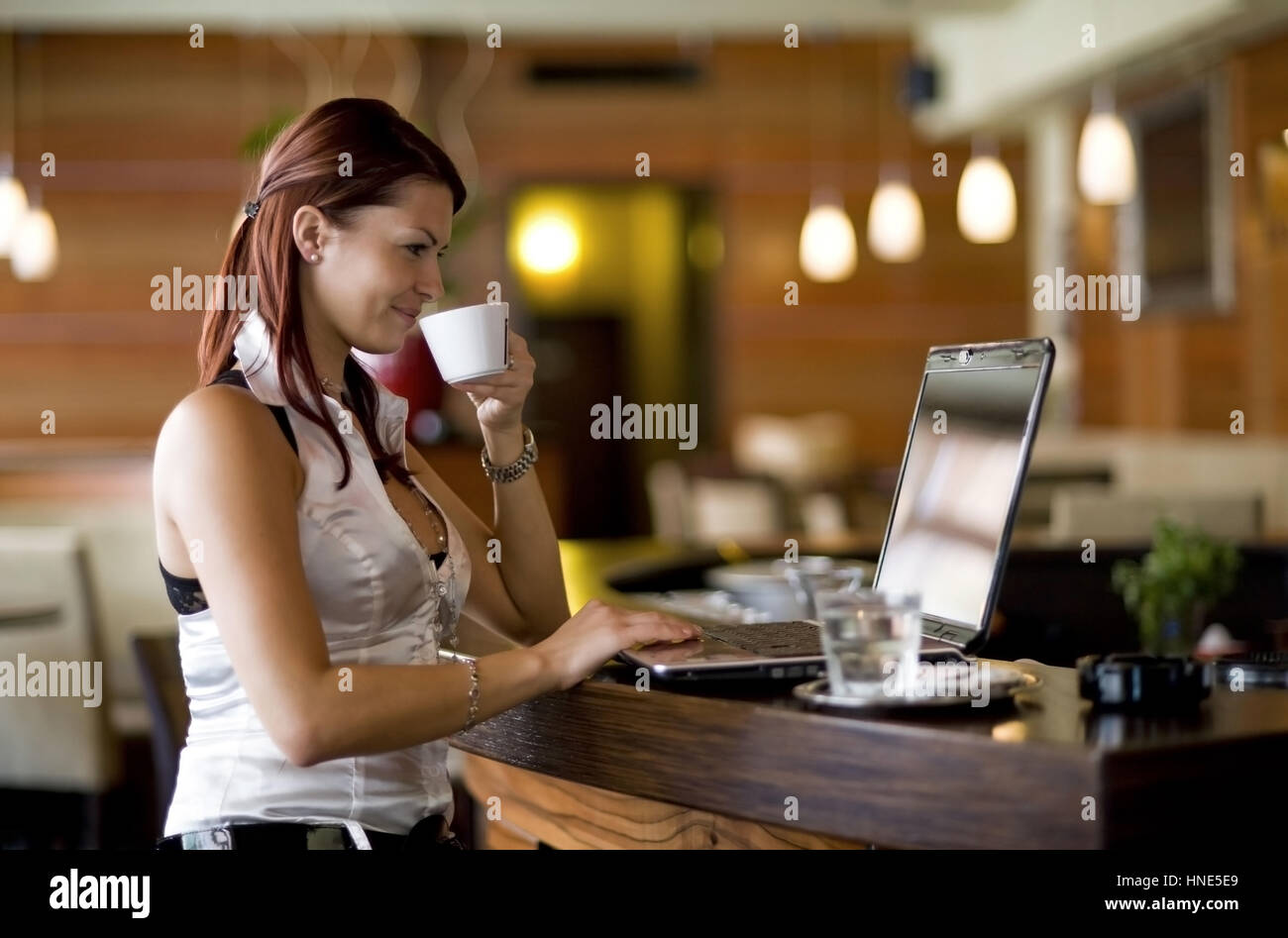 Communiqué de modèle, Junge Frau sitzt im Kaffeehaus an der Theke und arbeitet suis coffre - young woman using laptop in cafeteria Banque D'Images