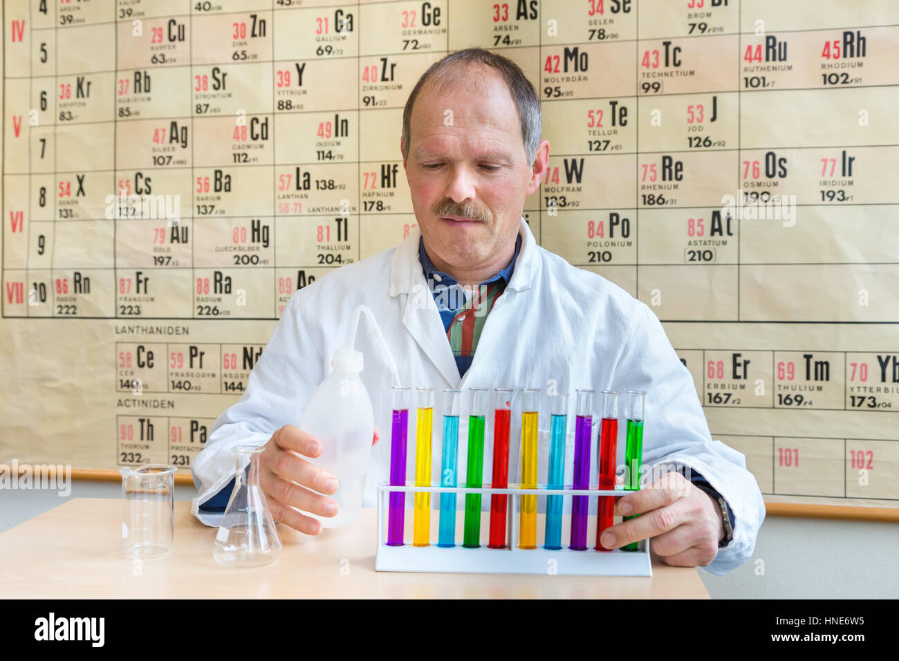 Chemist in lab coat couleur de remplissage des tubes à essai près de tableau périodique Banque D'Images