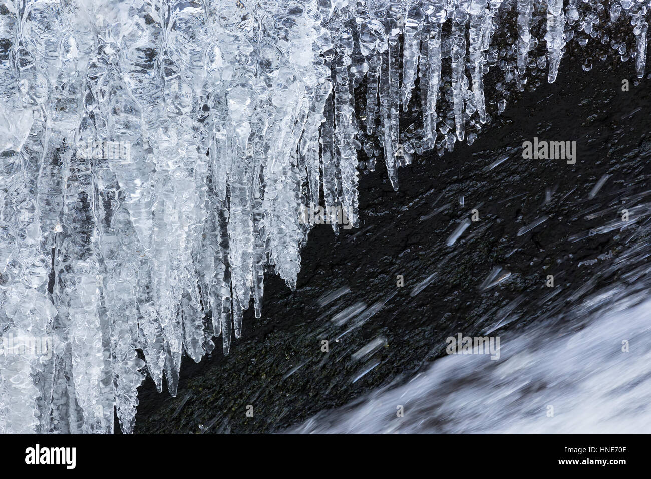 Glaçons suspendus au-dessus de l'eau congelée streaming de cascade en hiver Banque D'Images