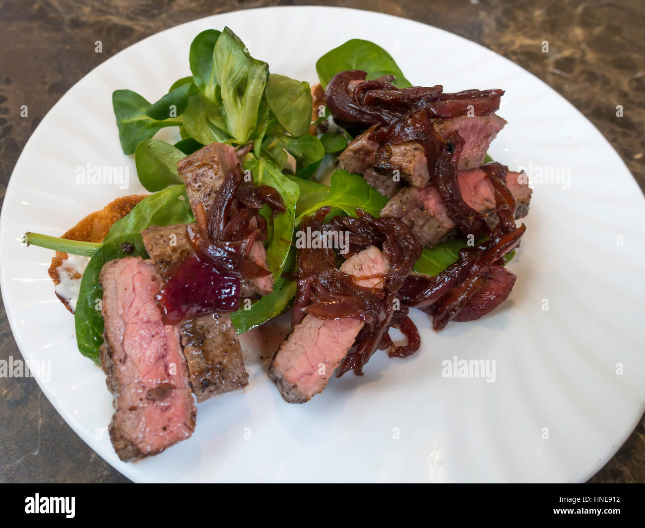 Steak Sandwich snack ouvert le midi servi avec oignons rouges caramélisés, mayonnaise au raifort et jeunes épinards Banque D'Images