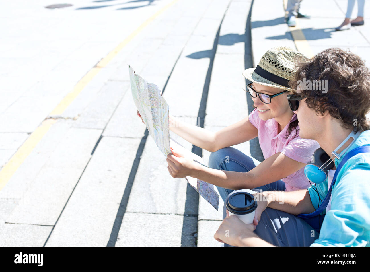 Heureux couple reading map while sitting on steps outdoors Banque D'Images