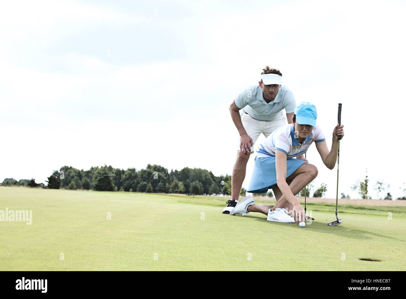 Homme avec femme visant ball on golf course contre le ciel Banque D'Images