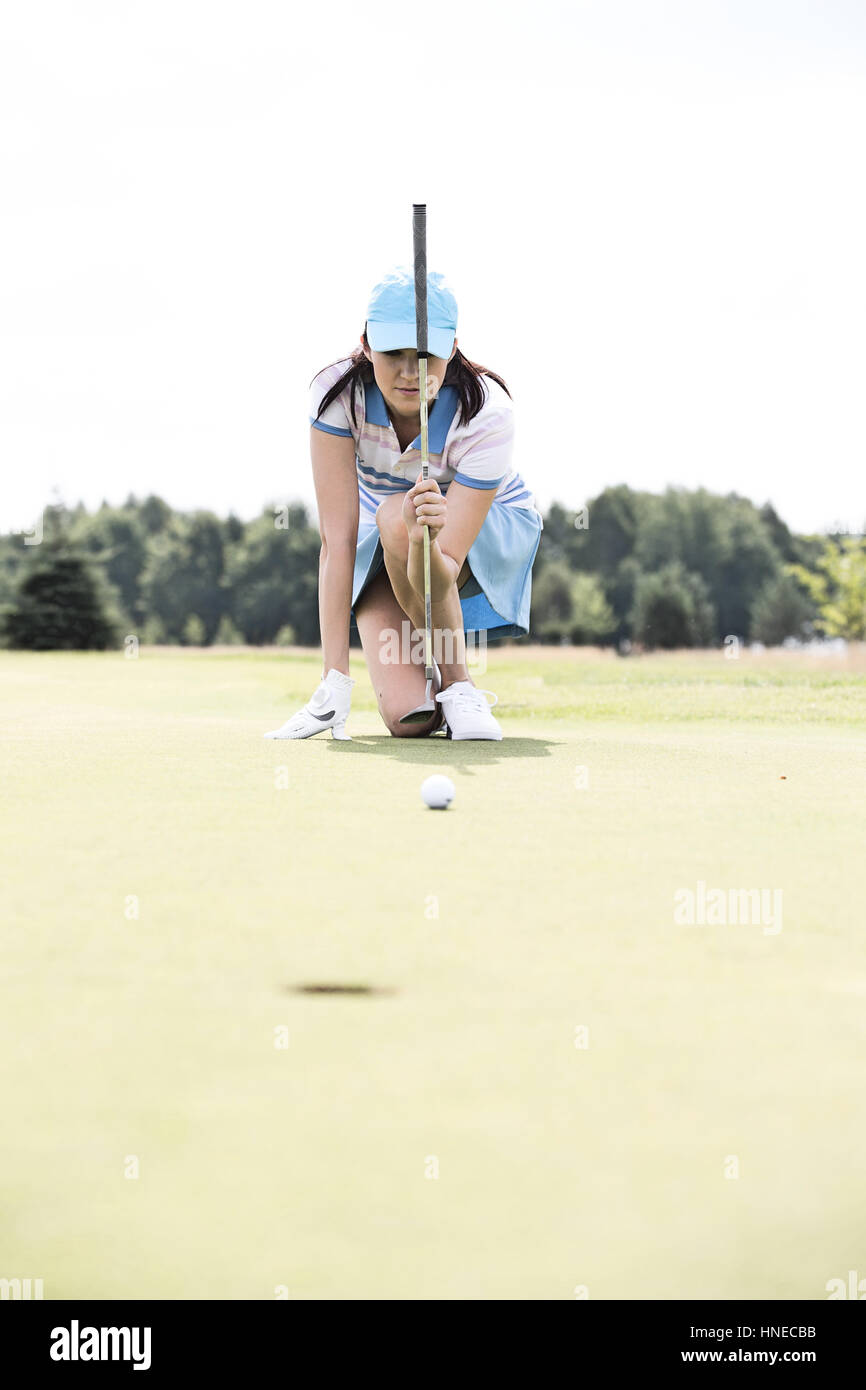 Jeune femme visant boule tout en s'agenouillant à golf course Banque D'Images