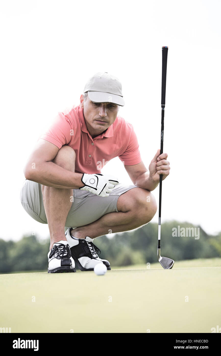 Homme d'âge moyen visant boule tout crouching on golf course Banque D'Images