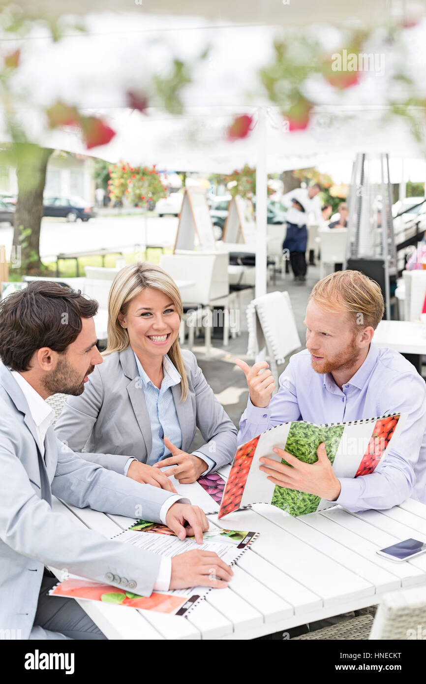 Portrait of happy businesswoman avec collègues masculins menu décider at sidewalk cafe Banque D'Images