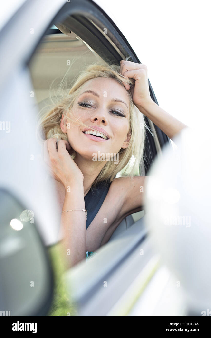 Happy young woman leaning on car window Banque D'Images