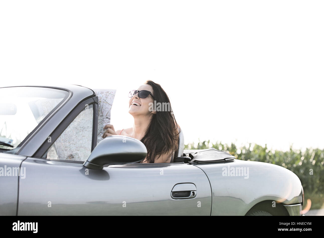 Happy woman holding map while sitting in convertible contre ciel clair Banque D'Images