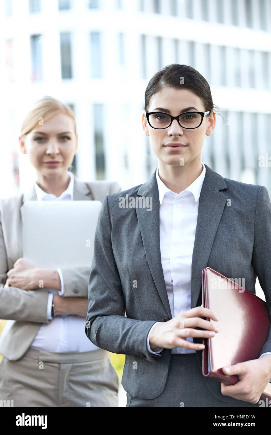 Portrait of businesswoman holding folder avec collègue en arrière-plan Banque D'Images