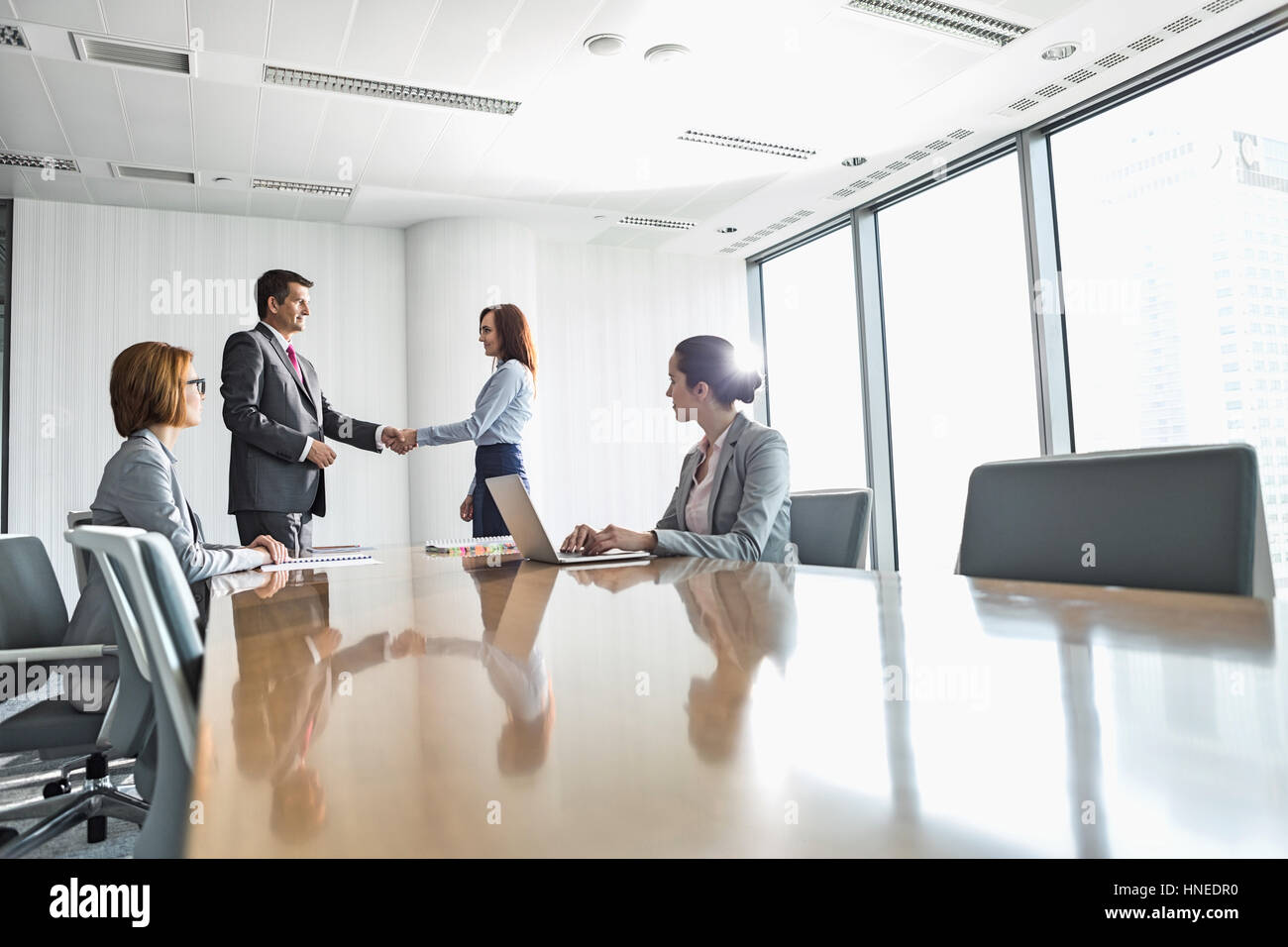 Businessman and businesswoman shaking hands in conference room Banque D'Images