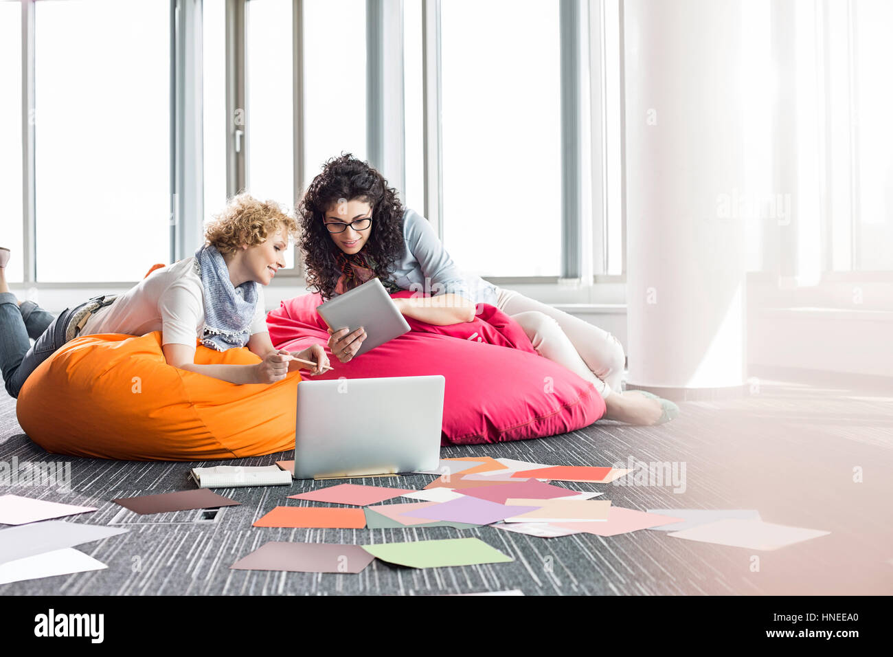 Les femmes d'affaires créatifs à l'aide de tablet PC tout en vous relaxant sur les chaises de bureau à pouf Banque D'Images