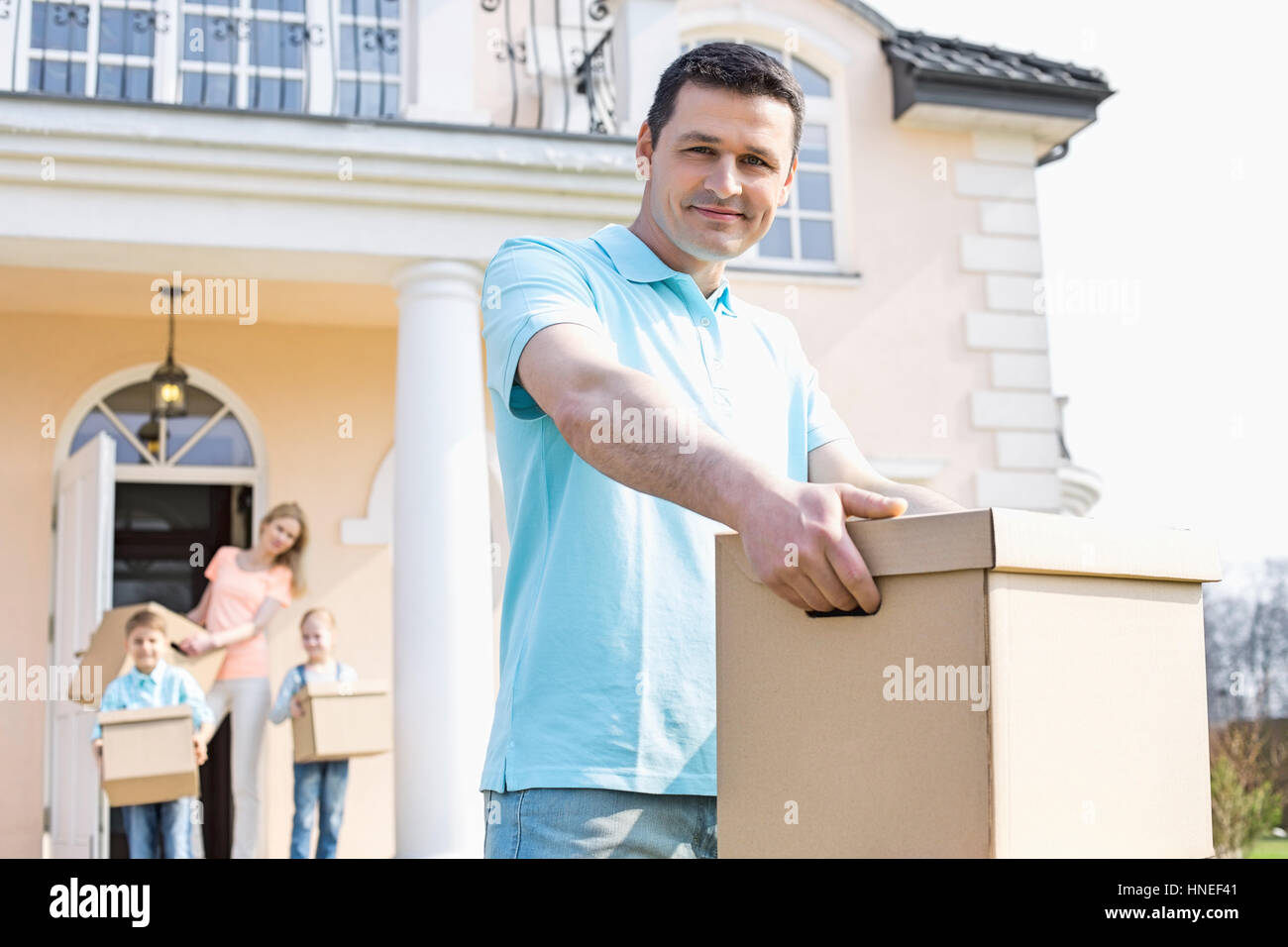 Portrait of man carrying cardboard box alors qu'un déménagement de la famille avec en arrière-plan Banque D'Images