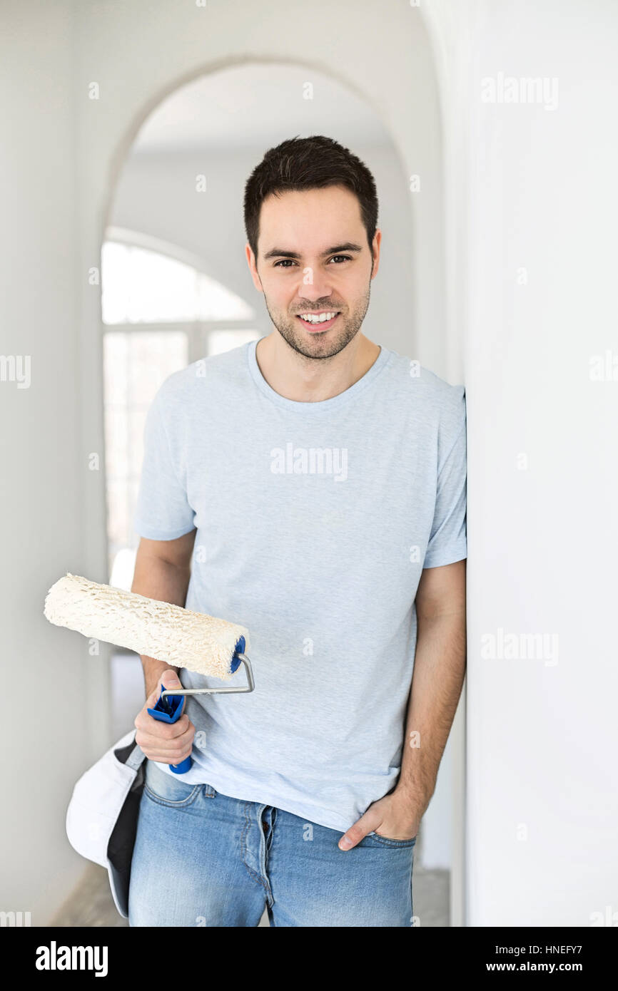 Portrait of handsome man holding paint roller in new house Banque D'Images
