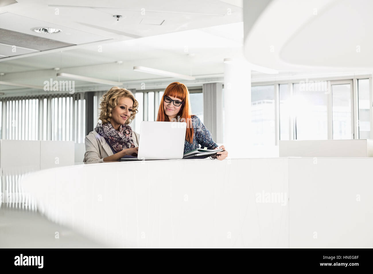 Les femmes d'affaires créatifs using laptop together in office Banque D'Images