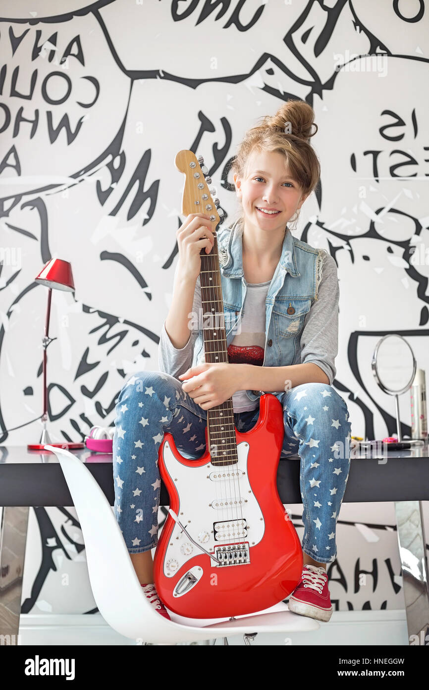Portrait en pied de fille avec une guitare électrique assis sur une table d'étude à la maison Banque D'Images