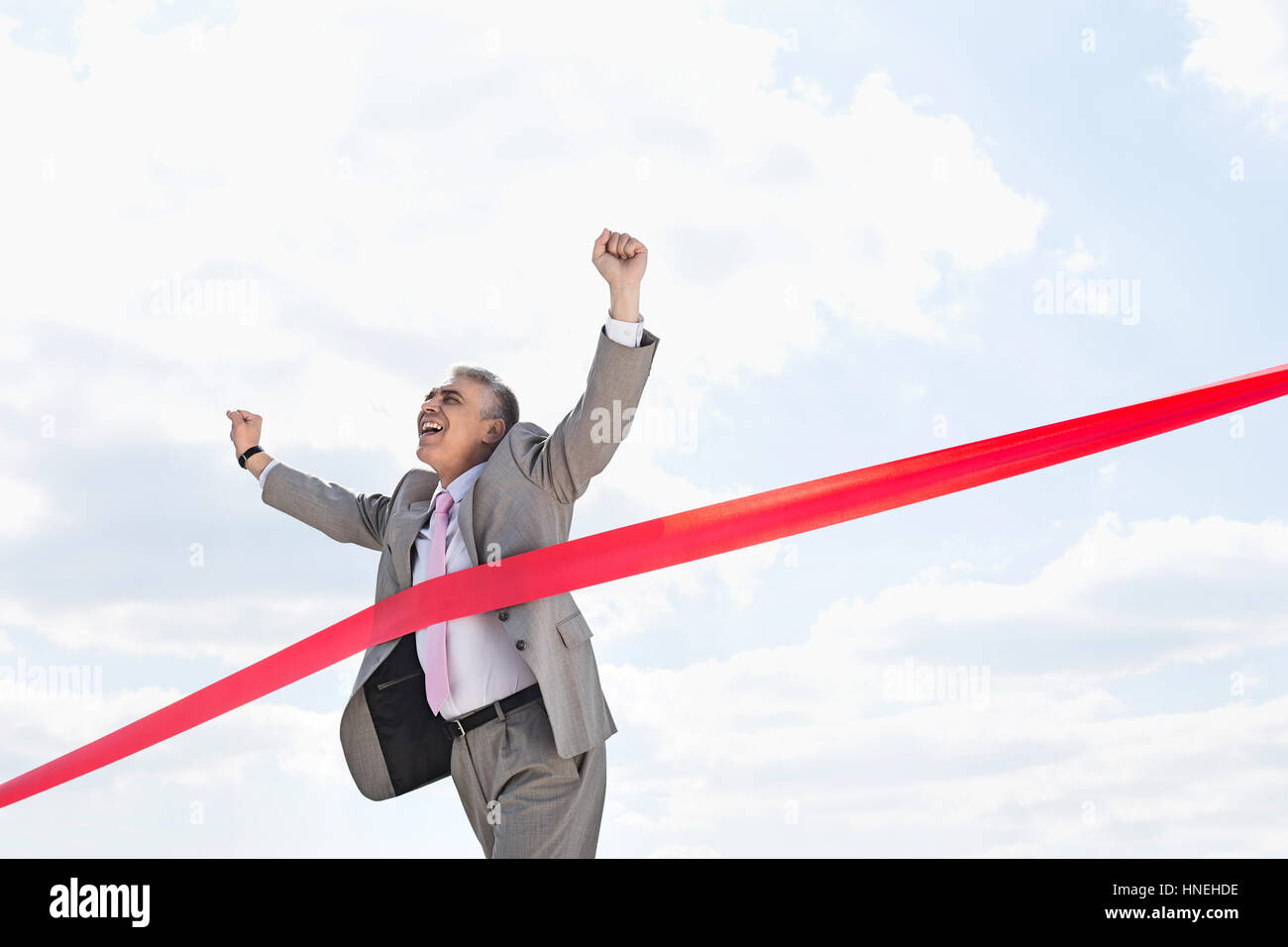 Cheerful businessman crossing finish line against sky Banque D'Images