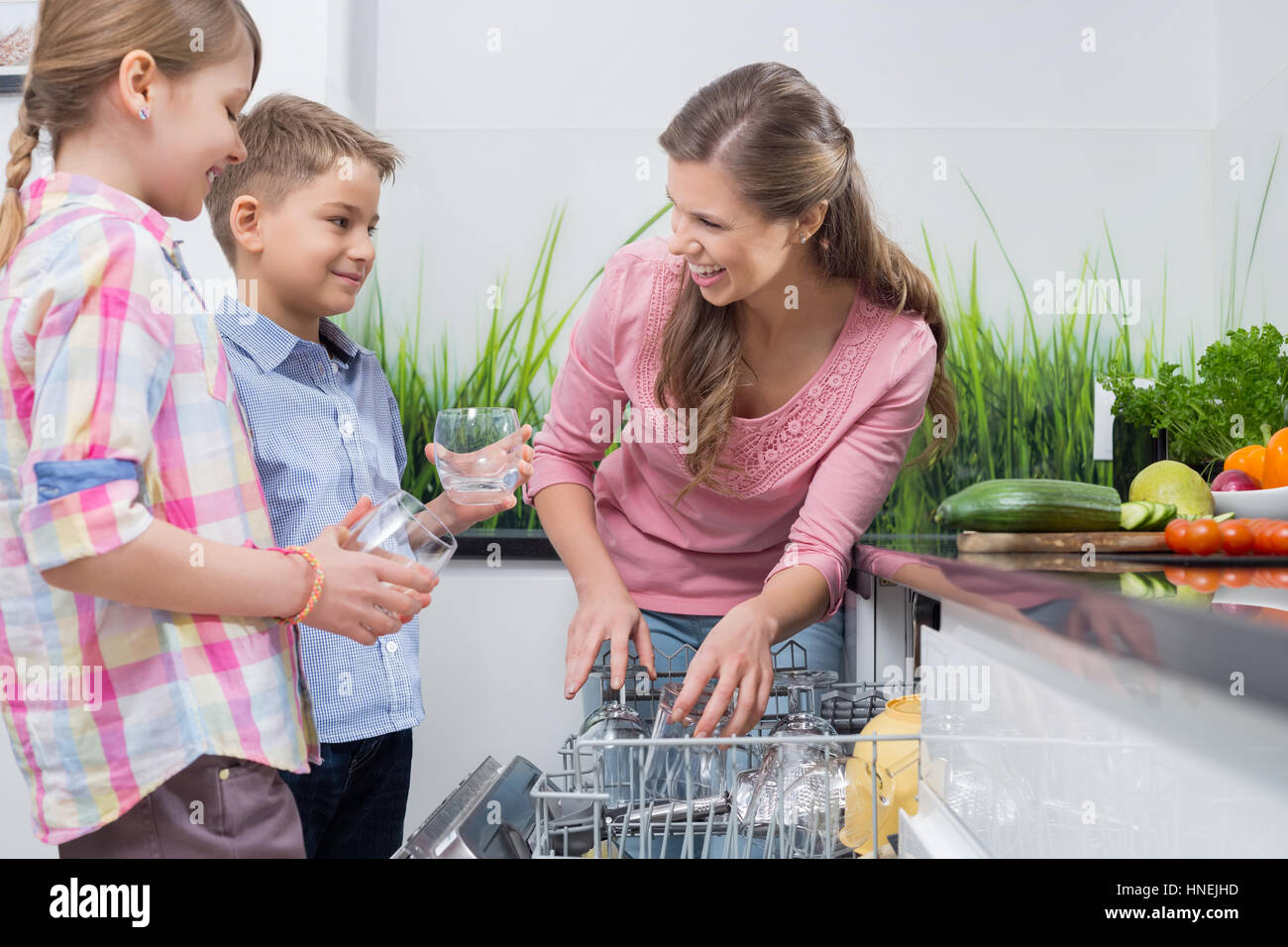La mère et les enfants heureux de placer dans le lave-vaisselle verres Banque D'Images