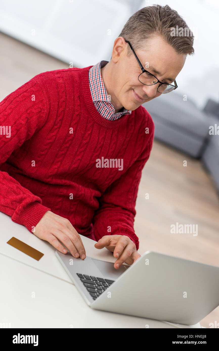 Mature man using laptop at table in house Banque D'Images