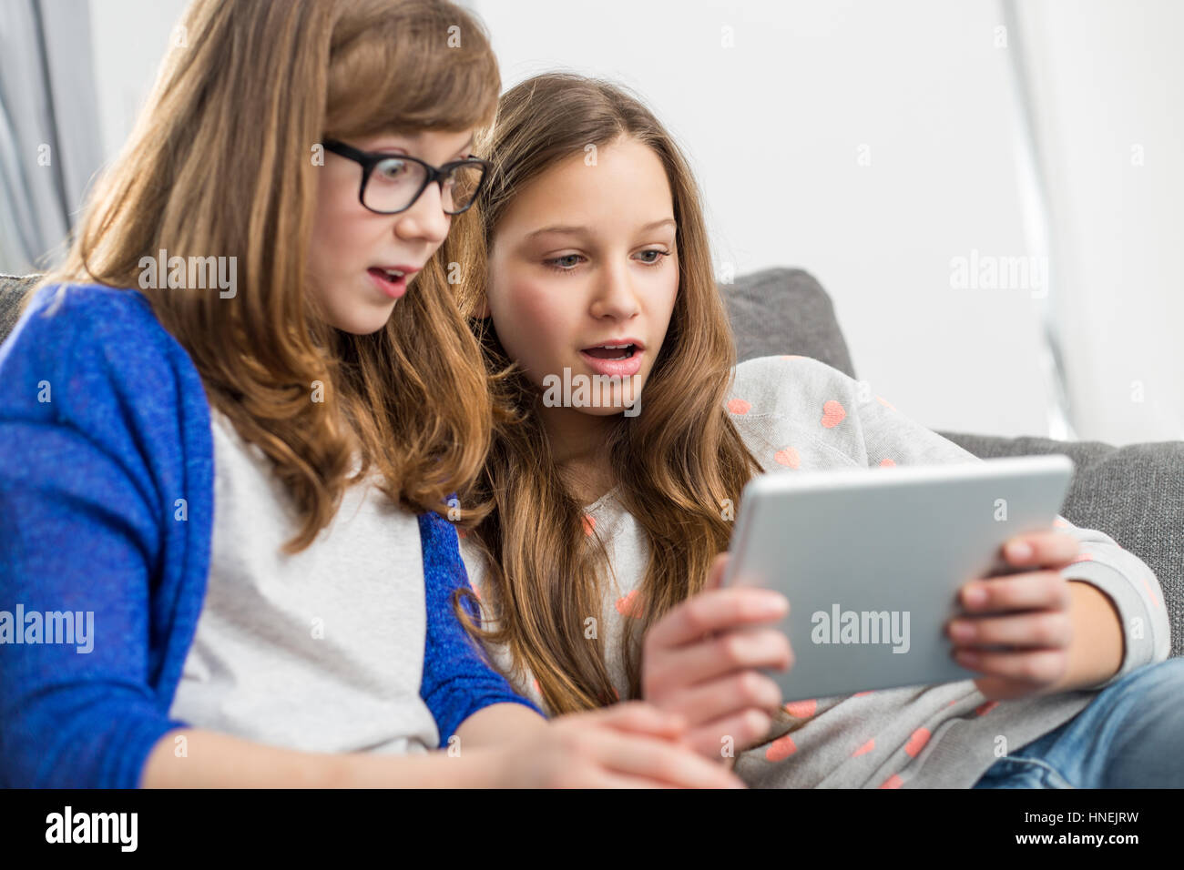 Choqué soeurs sitting on sofa at home Banque D'Images