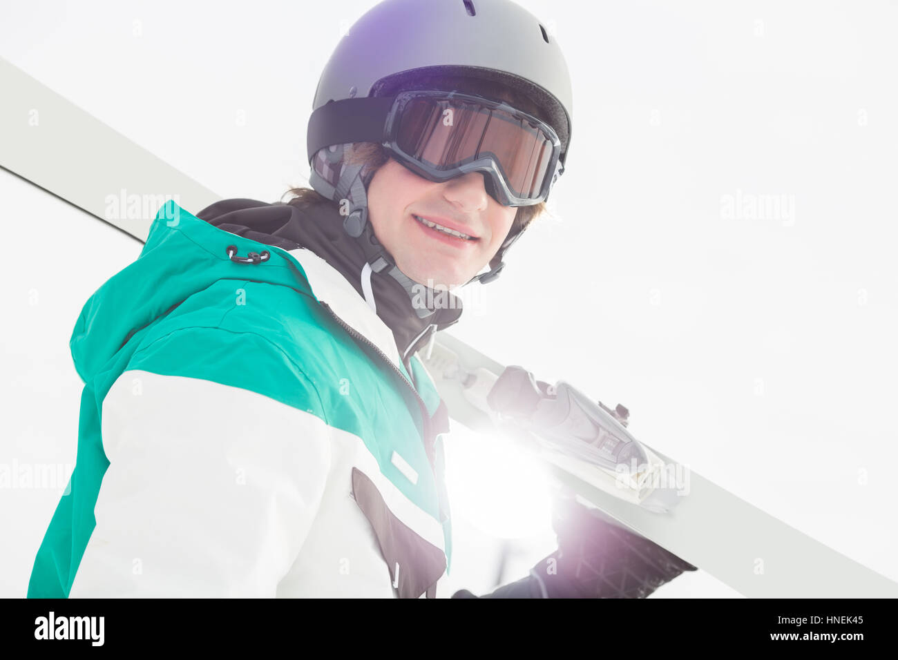 Portrait of smiling young man carrying skis contre ciel clair Banque D'Images