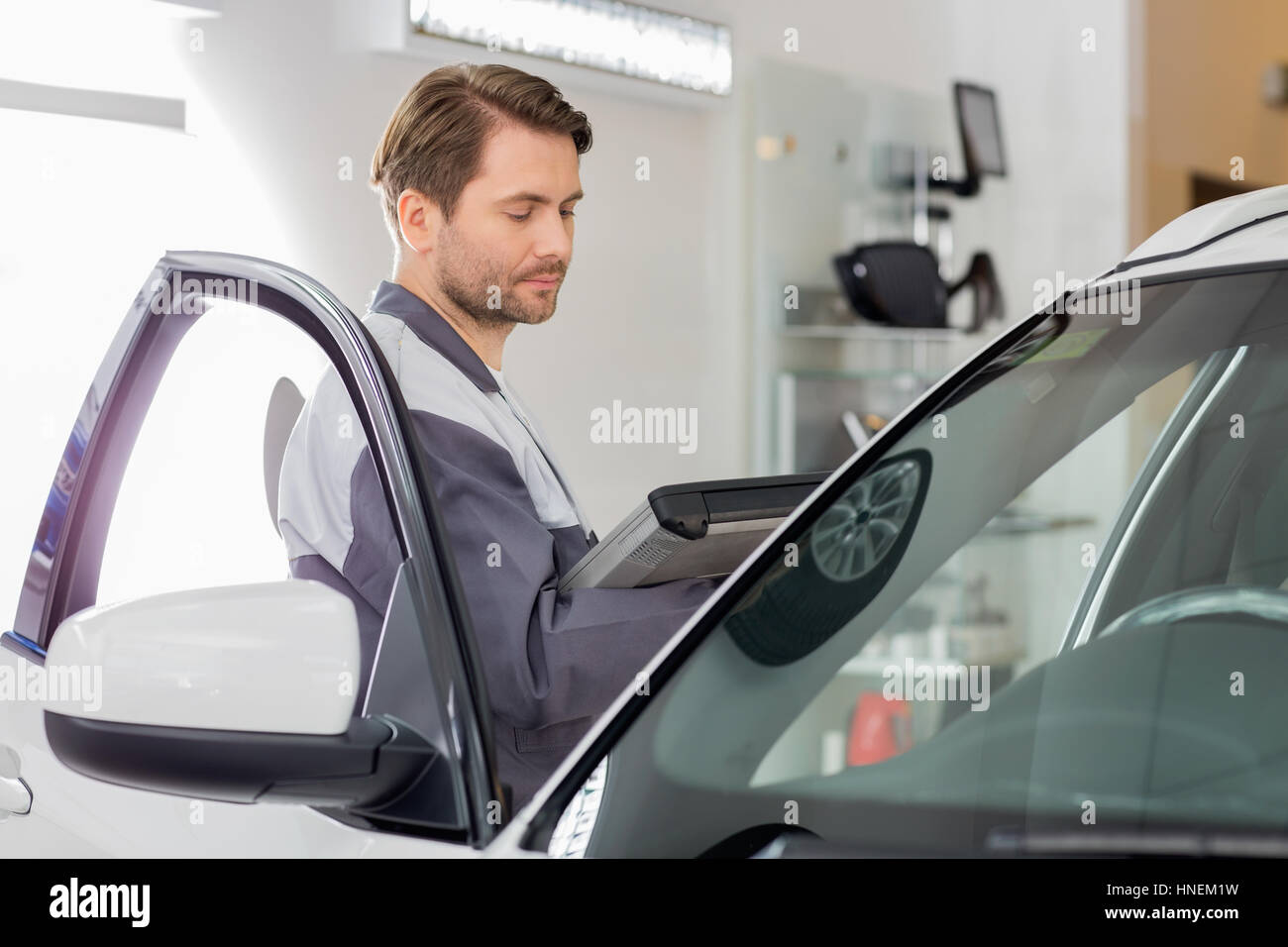Vue latérale du technicien d'entretien d'hommes holding tablet PC lors de l'examen de voiture en atelier Banque D'Images
