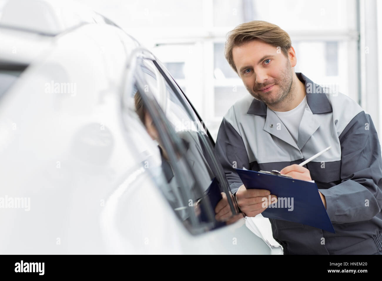 Portrait of smiling woman holding clipboard mécanicien automobile tout en s'appuyant sur la fenêtre de voiture en atelier Banque D'Images
