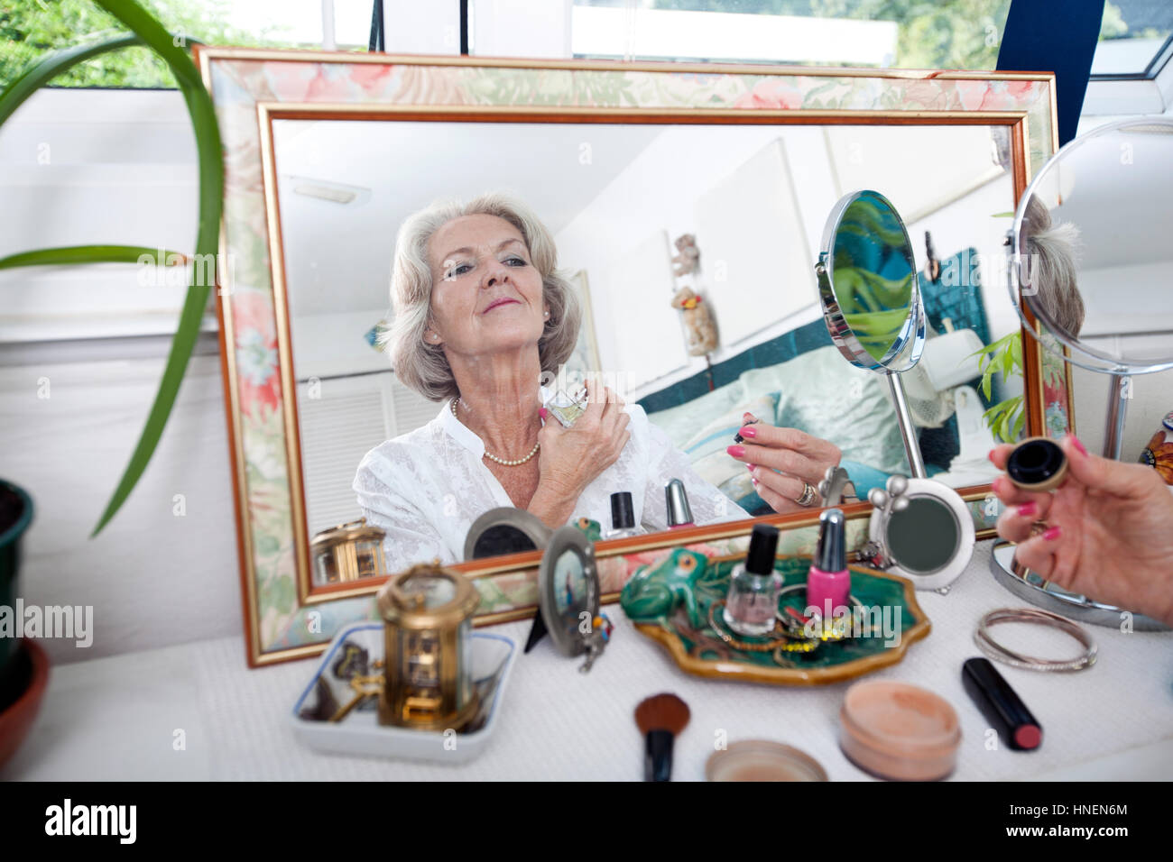 Reflet de miroir senior woman spraying perfume sur elle-même à la maison Banque D'Images