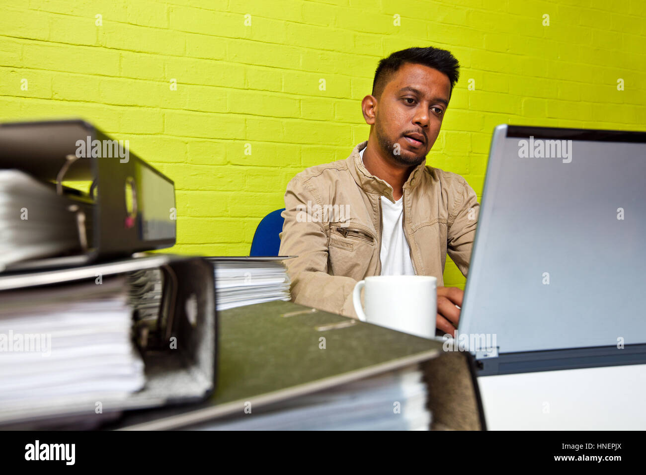 Jeune Indien homme travaillant à son ordinateur entouré par dossiers Banque D'Images