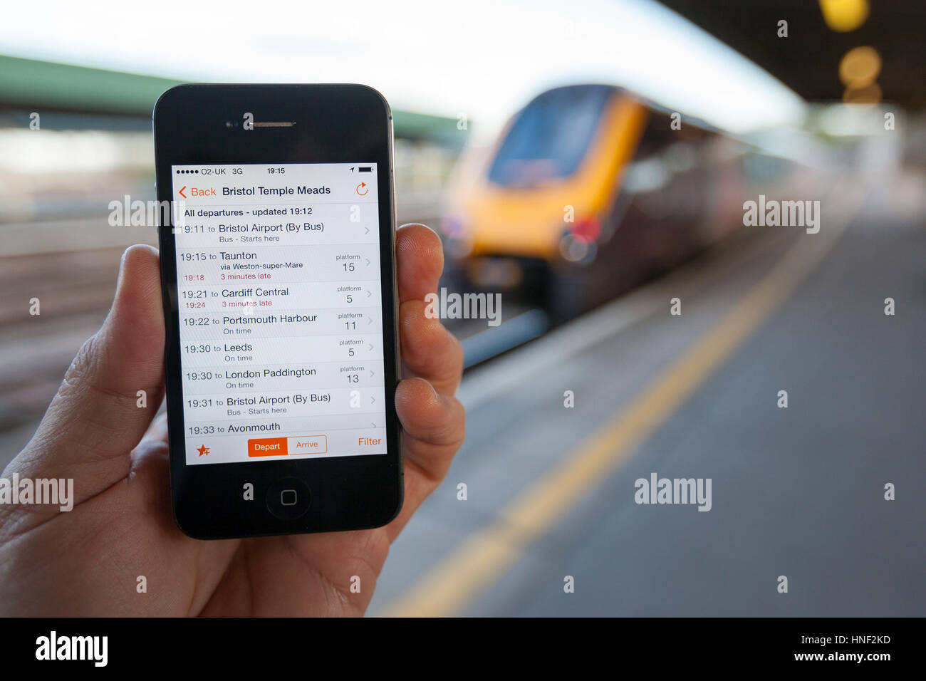 BRISTOL, UK - 8 avril 2014 : un mâle main tenant un iPhone à la gare de Bristol avec un train dans l'arrière-plan. Le téléphone intelligent affiche en tr Banque D'Images