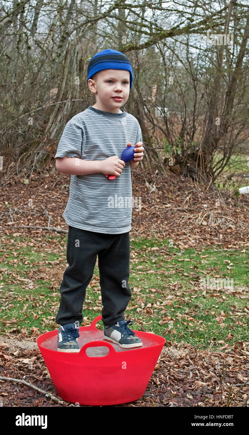 Ce portrait garçon de 5 ans joue à l'extérieur et debout sur un seau rouge  qui est gelée glace solide. Il porte un chapeau bas bleu, noir sweat Photo  Stock - Alamy