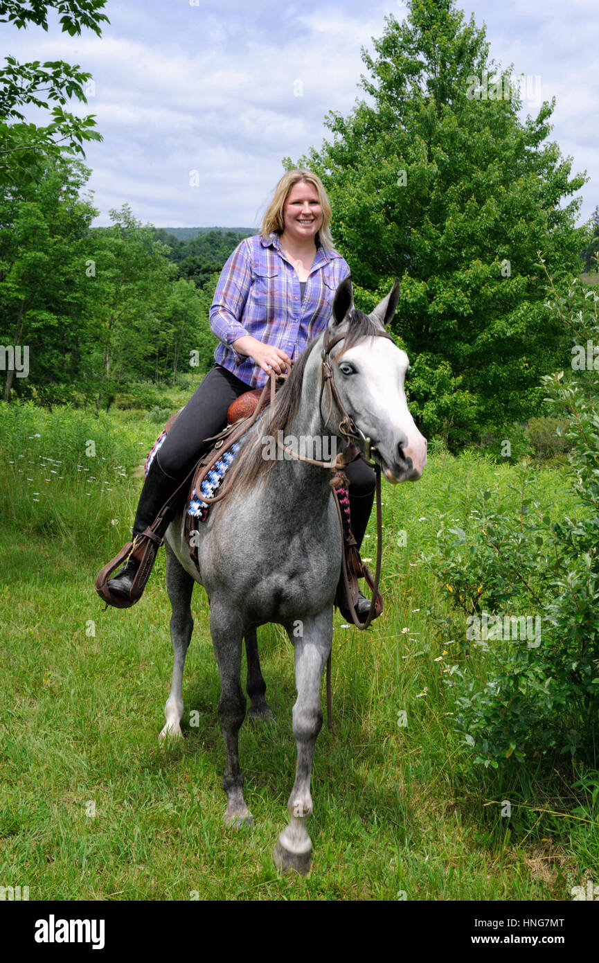 Femme aux cheveux blonds, dans les tenues, monté sur un blue-eyed,  white-faced, cheval pie, équitation western dans l'herbe des champs verts  de l'été le feuillage. PA Photo Stock - Alamy