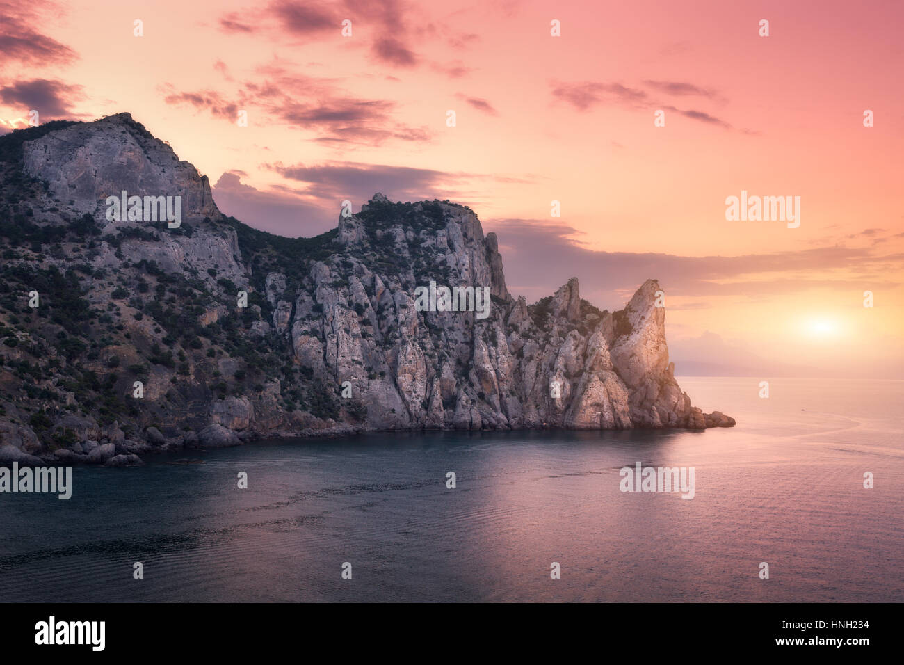 Montagnes colorées contre ciel nuageux au coucher du soleil. Paysage avec montagnes, mer, ciel rouge et jaune soleil. La nature et les voyages au crépuscule. Nuages floue Banque D'Images