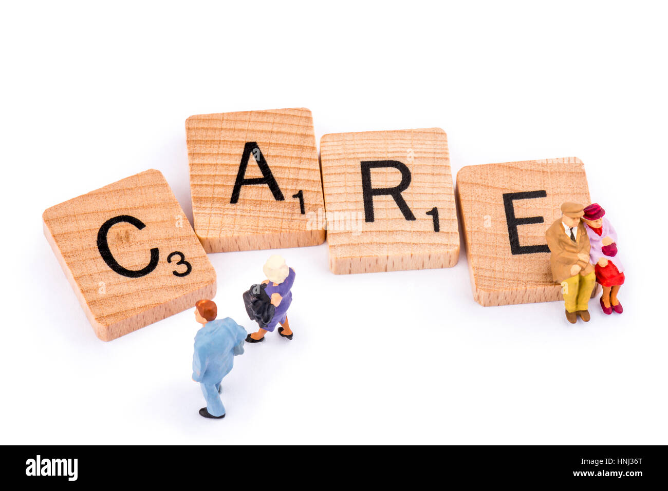 Scrabble lettres forment le mot soin. Un couple de personnes âgées s'asseoir sur la lettre E du mot soins comme un couple plus jeune à pied. Banque D'Images