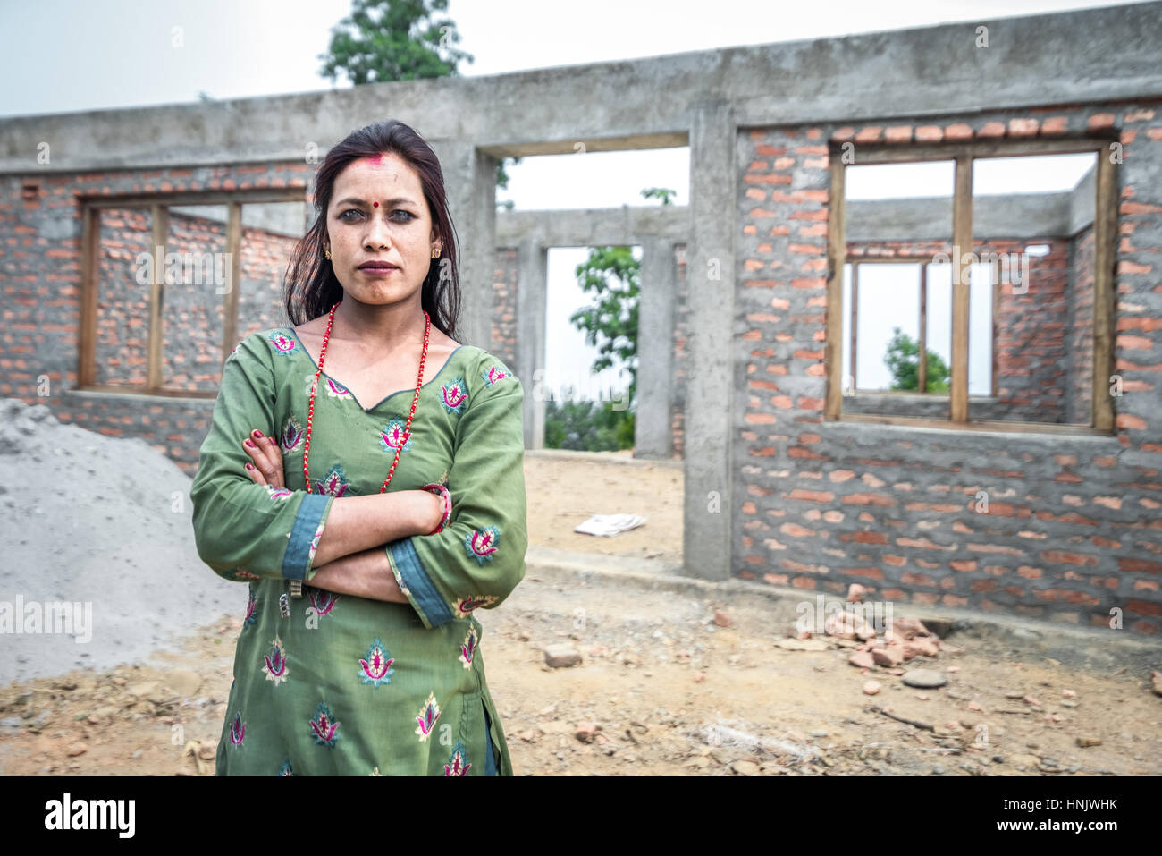 Une femme pose pour appareil photo en face d'une maison inachevée pour la 2015 victimes du séisme en Chandani village Mandan, Kavrepalanchowk, Népal. Banque D'Images