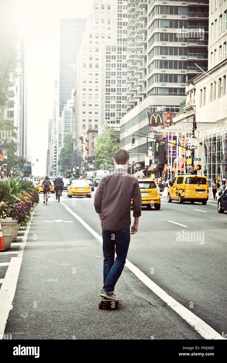 Jeune homme avec skateboard de derrière dans le centre de Manhattan à New York City, USA. Banque D'Images