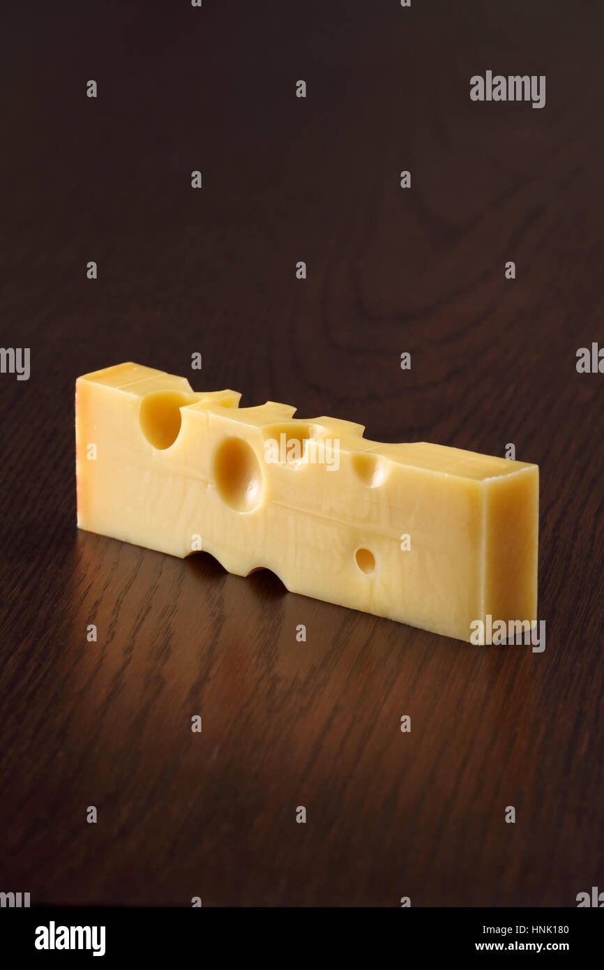Photo d'un bloc de fromage Emmental de Suisse sur une table en bois sombre. Banque D'Images