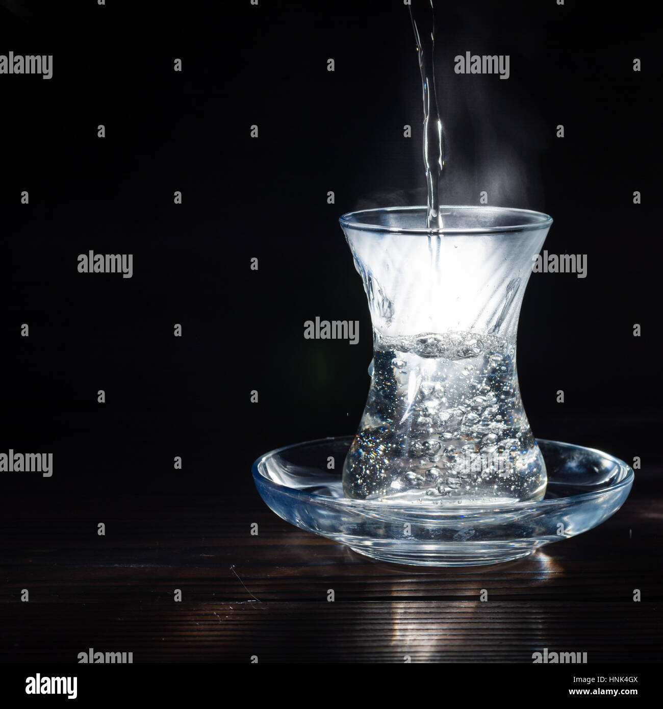 Tasse en verre transparent avec de l'eau bouillante dans la houle. La vapeur par le haut. Fond noir. L'espace pour le texte. Banque D'Images