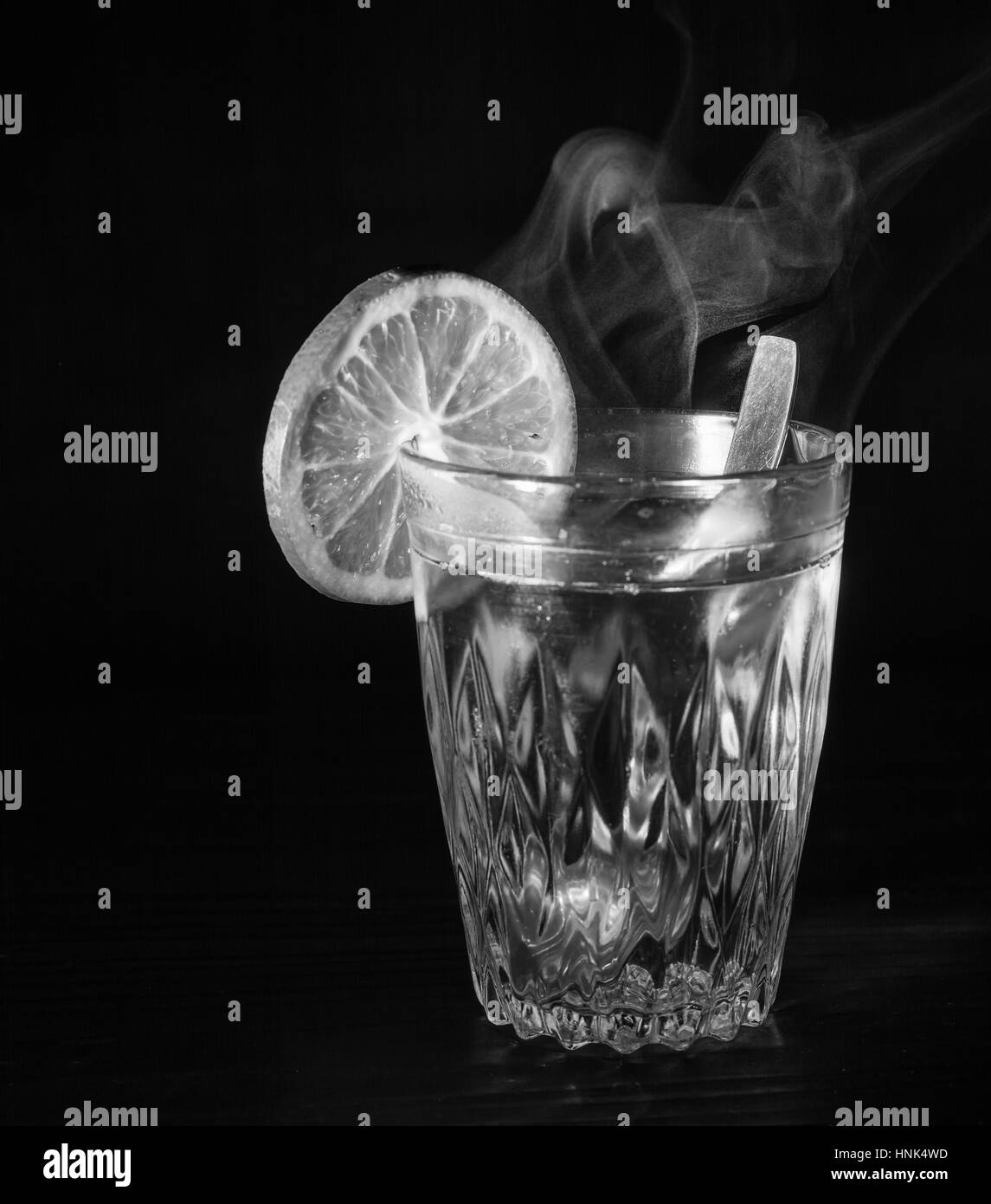 Tasse en verre transparent avec de l'eau bouillante dans la houle. La vapeur par le haut. Fond noir. L'espace pour le texte. Banque D'Images