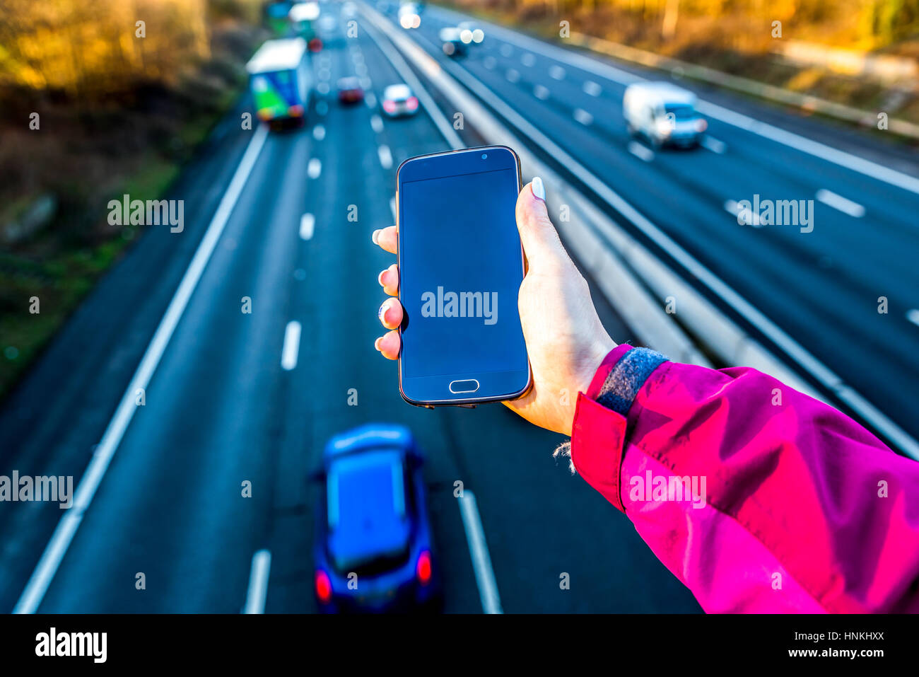 La vue quotidienne de woman holding smartphone au Royaume-Uni l'autoroute. Banque D'Images