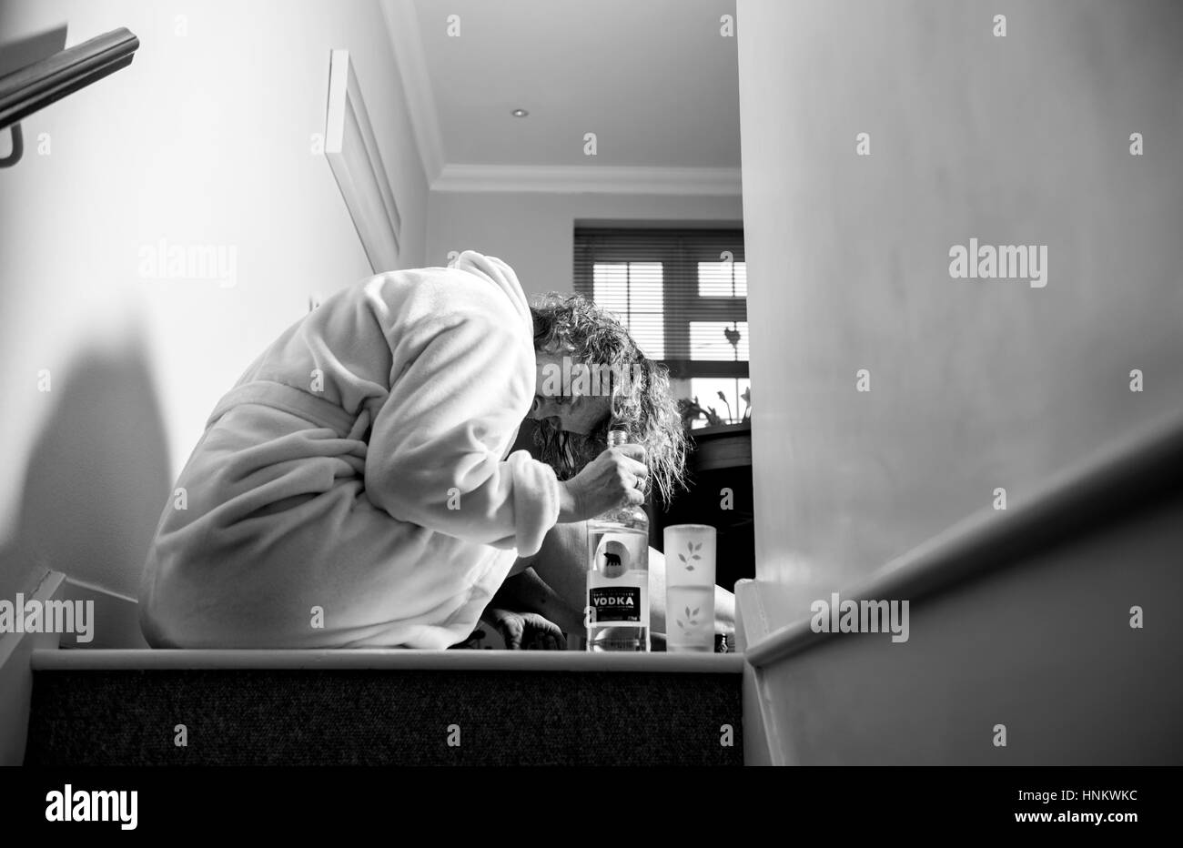 Femme assise enfoncée dans sa robe de chambre à la maison pendant la journée à boire fortement traiter eux-Photographie - posée par model Banque D'Images