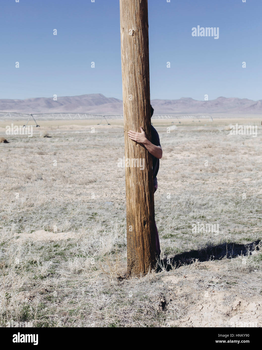 L'homme avec ses bras autour d'un poteau en bois utliities, accroché à l'étreindre ou poster dans un paysage ouvert. Banque D'Images